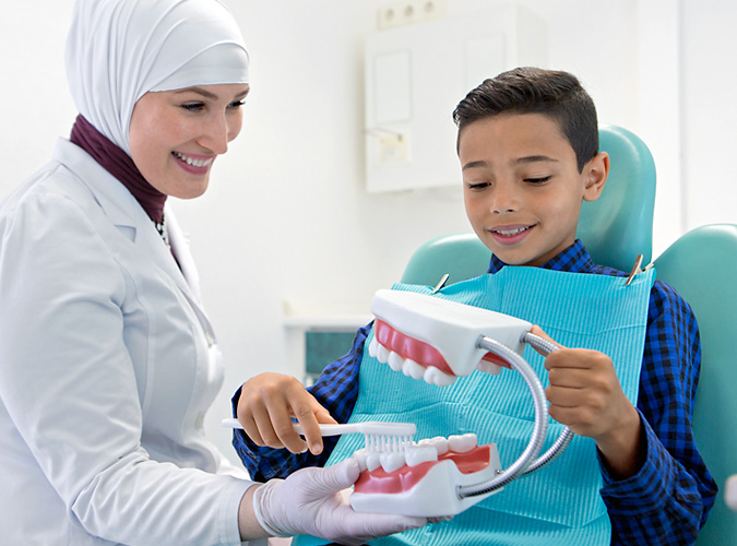 Zahnärztin Luma erklärt kleinen Patient das richtige Putzen der Zähne.